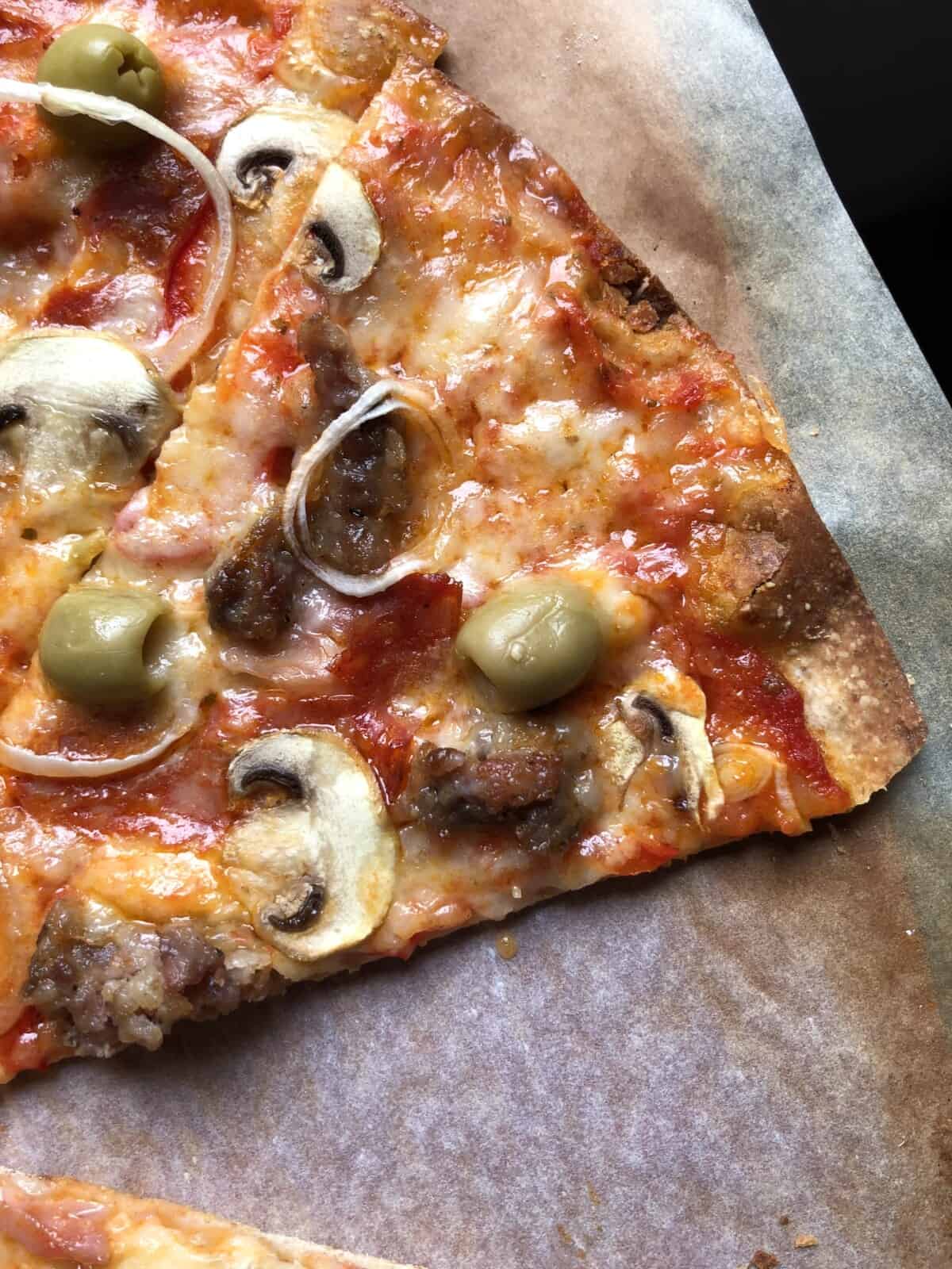 closeup of Super crispy sliced whole wheat Supreme pizza with green olives, spicy ventricina salami, salsiccia, prosciutto cotto, mushrooms, red bell peppers, and onions.
