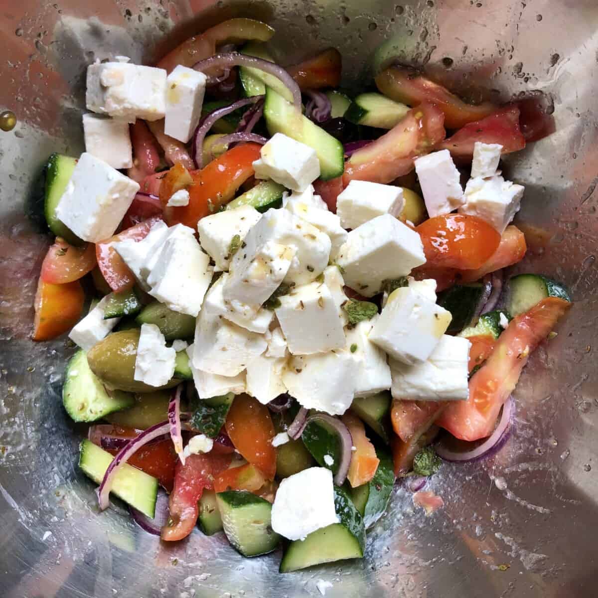 Chopped and sliced veggies with olives in a large mixing bowl tossed with the dressing and topped with feta cheese.