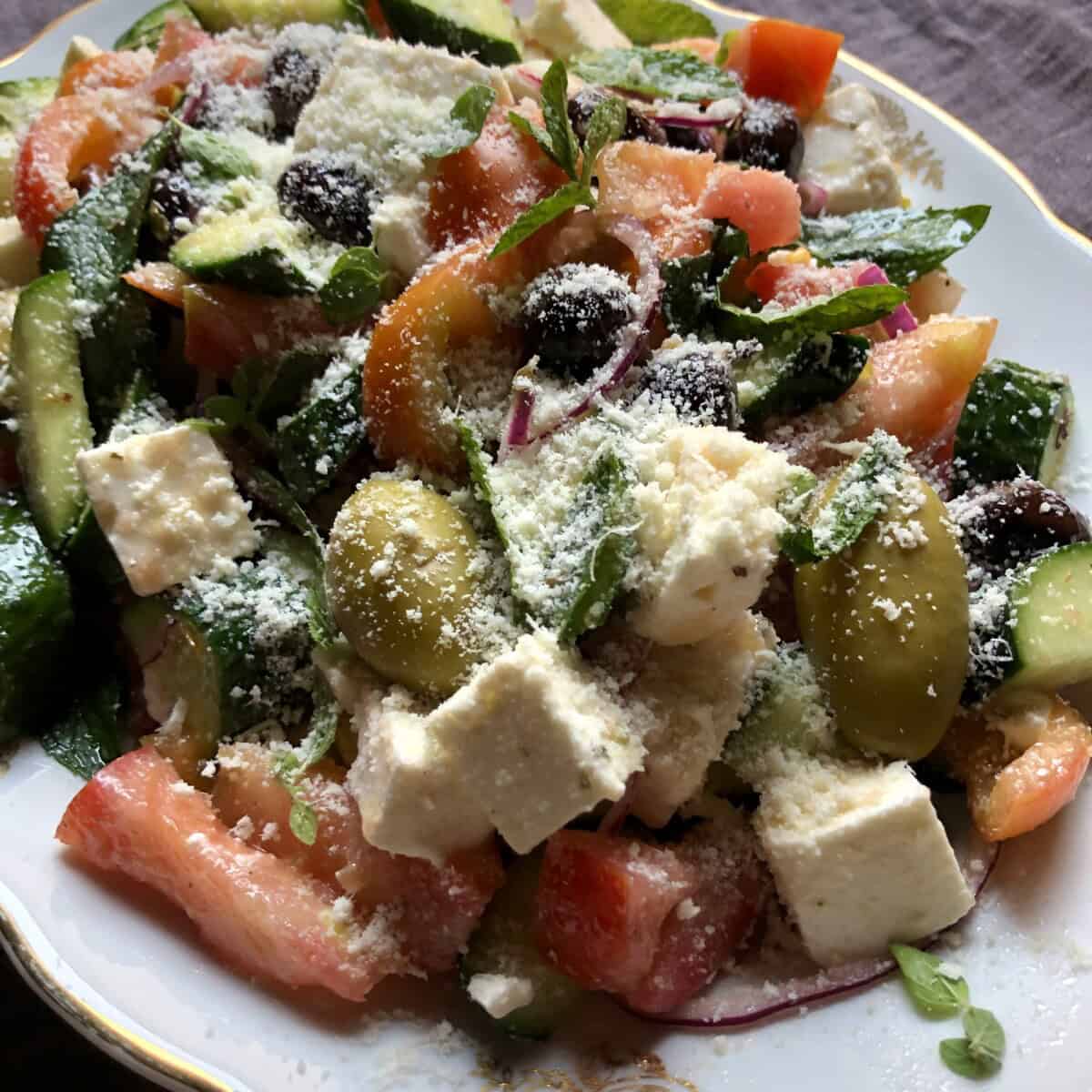 Large Greek salad piled high on a serving platter and sprinkled with grated parmesan cheese.