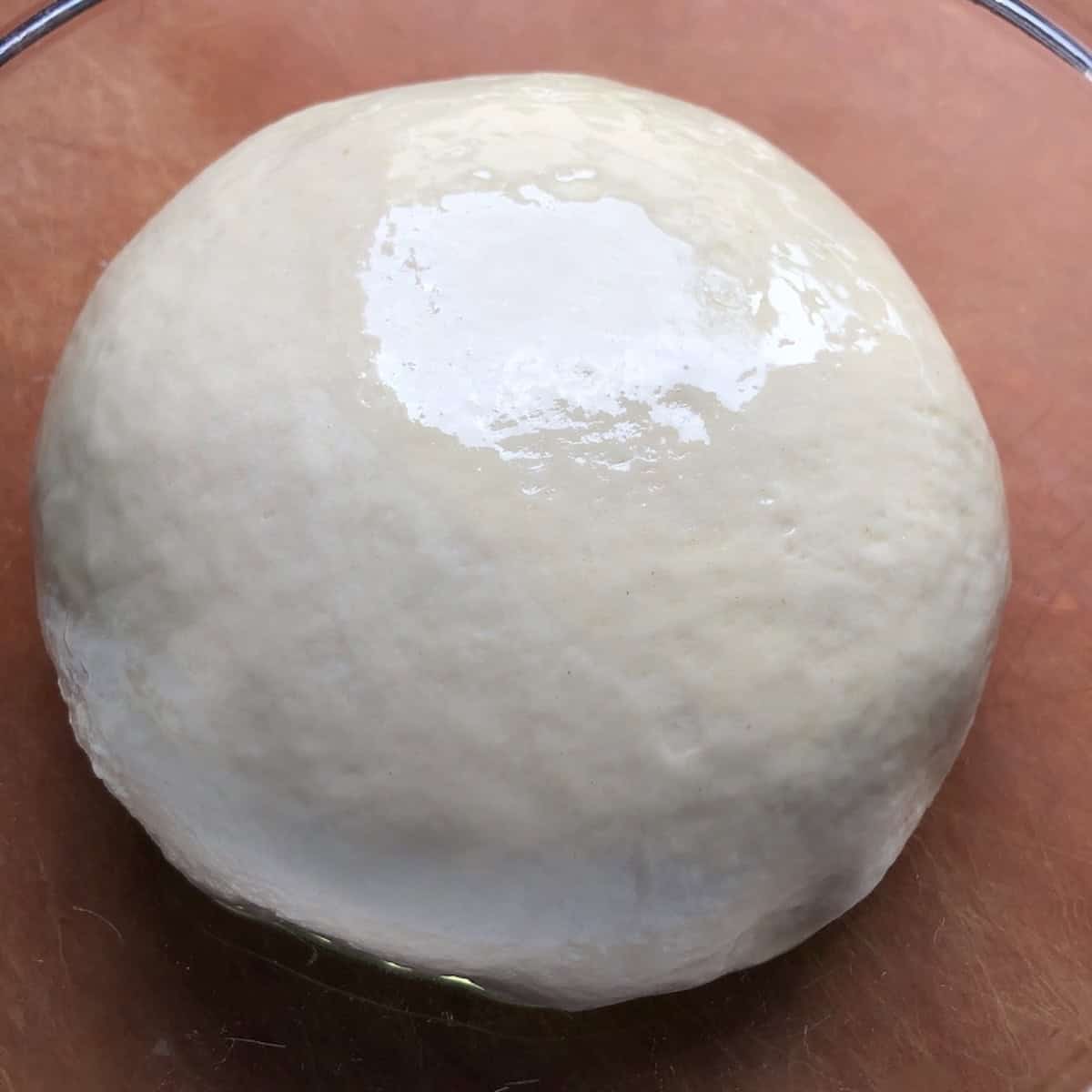 Oiled bread flour pizza dough ball placed in a lightly oiled bowl for its first rise, best pizza dough recipe with yeast for a soft fluffy pizza dough from scratch.
