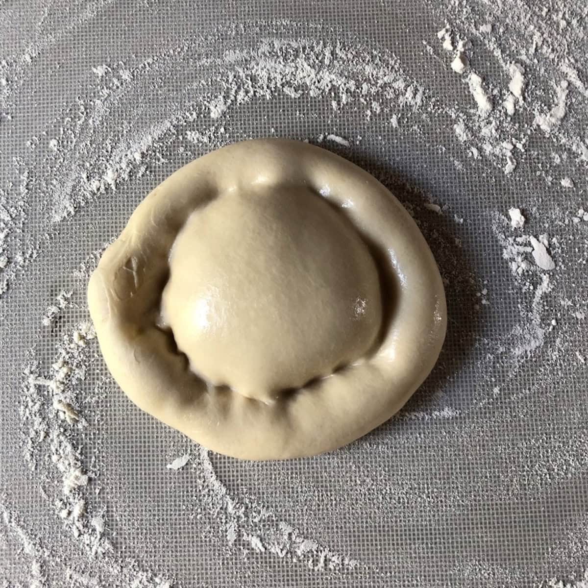 Bread flour pizza dough on a flour-dusted mat with a puffy cornice rim shaped by hand, showing how to make pizza dough with a light and airy crust before hand stretching the center ready to top, fluffy pizza dough recipe from scratch.
