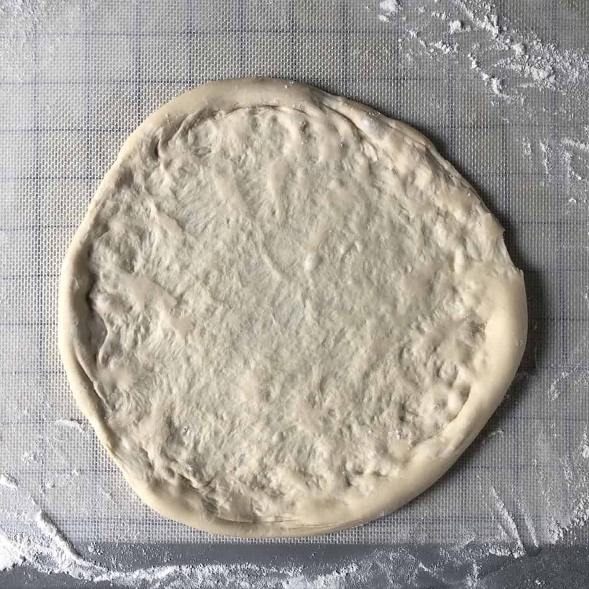 Hand stretched bread flour pizza dough with a fluffy puffy crust rim, ready for sauce on a homemade pizza dough from scratch using bread flour for pizza dough.
