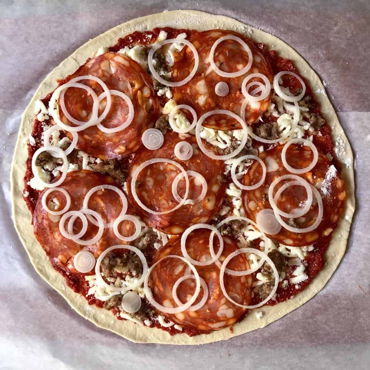 Unbaked pepperoni sausage and onion pizza topped and ready for the oven on a bread flour pizza crust, homemade pizza dough with bread flour for an easy pizza crust recipe.
