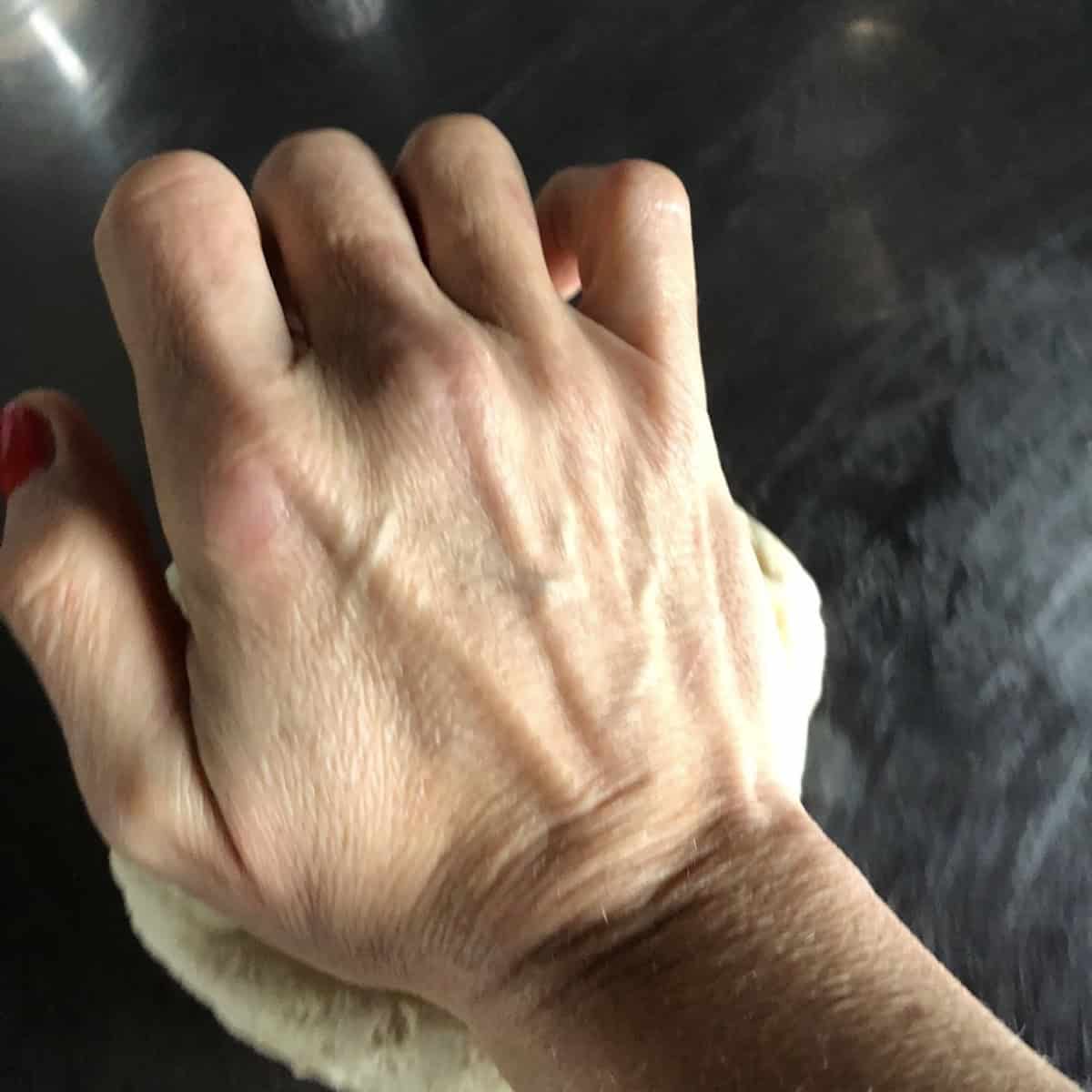 Hand kneading bread flour pizza dough on a lightly floured surface, showing how to knead pizza dough by hand for a crispy, tender, chewy homemade pizza dough recipe with bread flour.