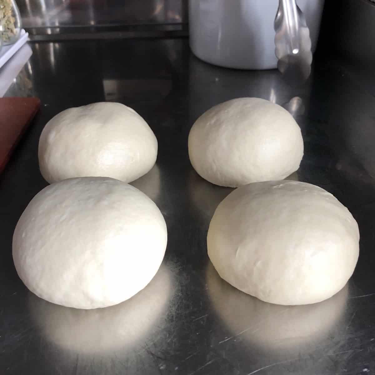Four perfectly formed bread flour pizza dough balls ready for their second rise, king arthur bread flour pizza dough recipe for soft chewy homemade pizza crust with crispy edges.