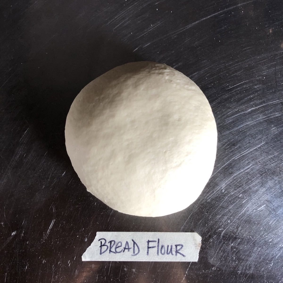 A perfectly kneaded bread flour pizza dough ball with a smooth matte surface ready for its first rise, pizza dough recipe with yeast using bread flour for the best pizza dough texture.
