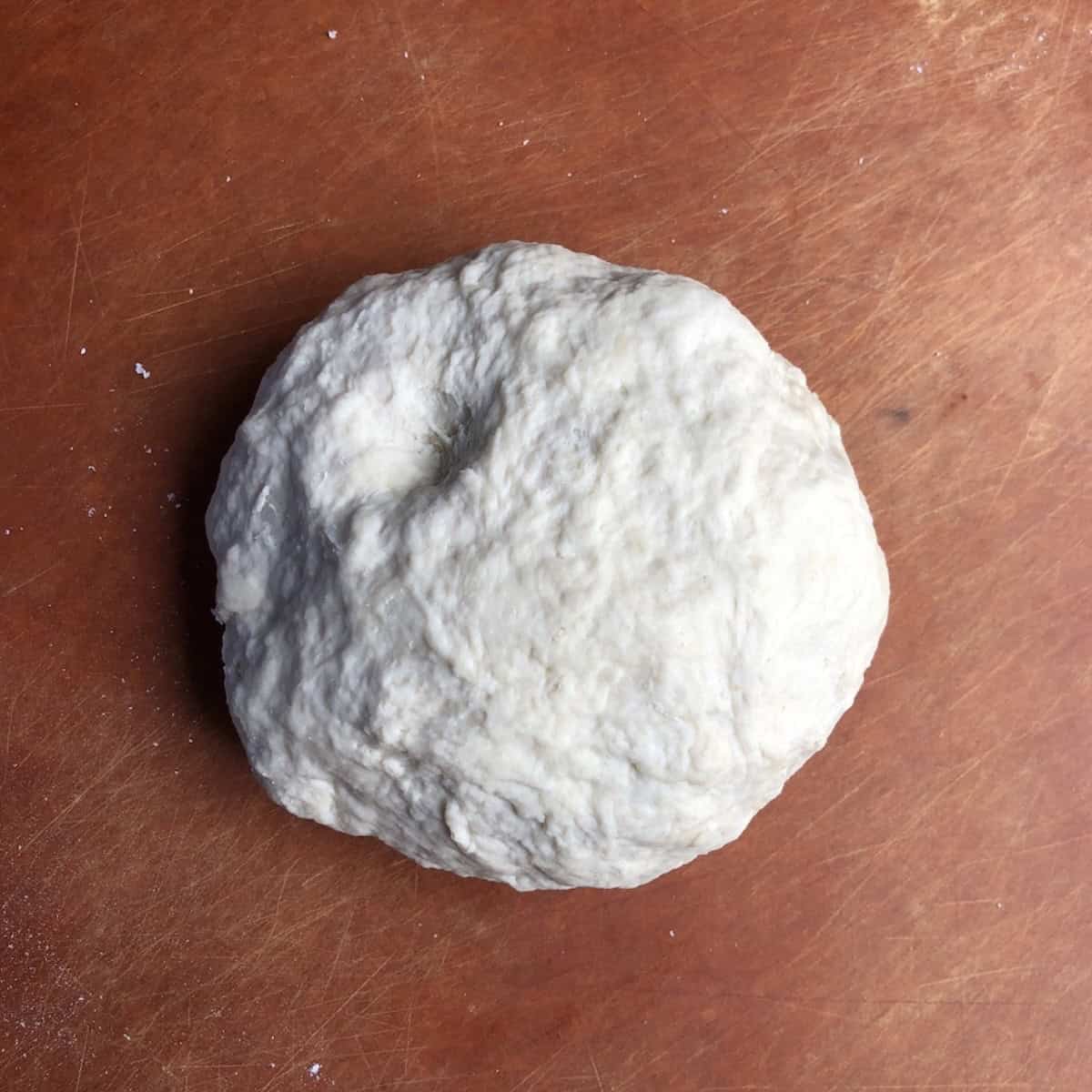 Shaggy bread flour pizza dough ball after combining dry ingredients with warm water, showing how do you make pizza dough from scratch with bread flour before kneading into a smooth dough.
