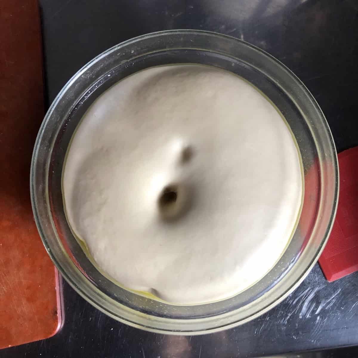 A finger poked into risen bread flour pizza dough with the hole remaining showing the dough is ready to punch down, how to make king arthur bread flour pizza dough recipe at home showing a simple pizza dough recipe. 
