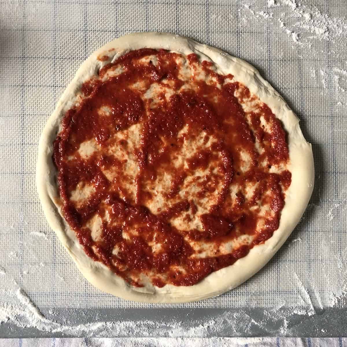 Easy pizza dough recipe with bread flour spread with homemade pizza sauce and ready for cheese and toppings, soft chewy pizza dough with a puffy crust made from scratch.
