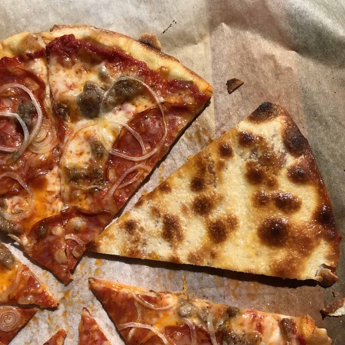 Crispy pepperoni sausage and onion pizza sliced and ready to serve, showing the underside of the pizza crust and how crispy it in this homemade pizza crust with king arthur bread flour.
