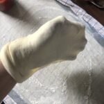 My hand in the center of the pizza dough with it wrapped around my whole hand as I toss it from one hand to another to stretch the dough.