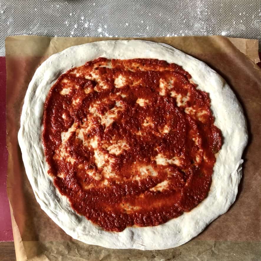 Thick crust pizza dough stretched and pizza sauce added to it.
