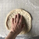 My hand pressing down on the larger dough to get it big enough to start hand-tossing it.