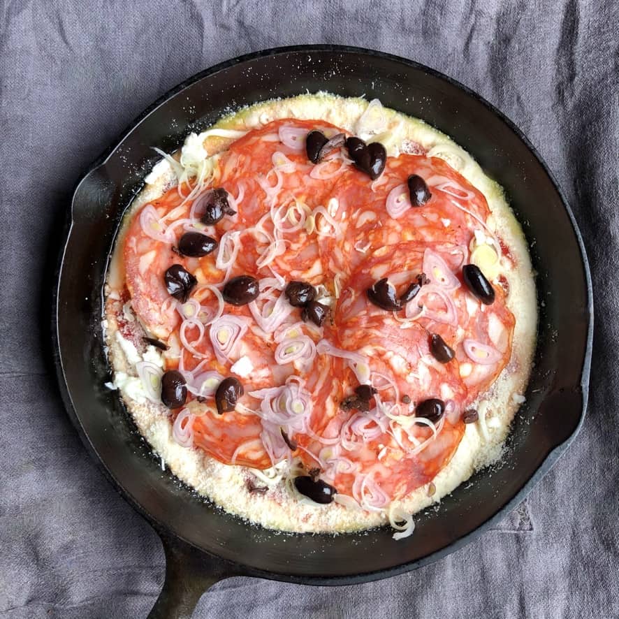 A thick-crust pan pizza in a cast iron skillet ready to be baked.