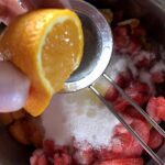 squeezing fresh orange juice into the jam mixture of fruit and sugar.
