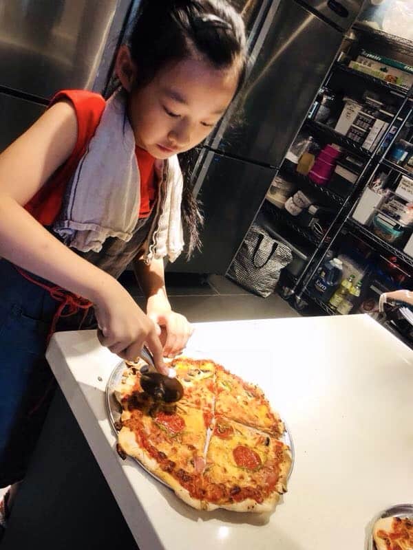 A young girl cutting her homemade thin-crust pizza she made in my kids pizza cooking course using this dough.