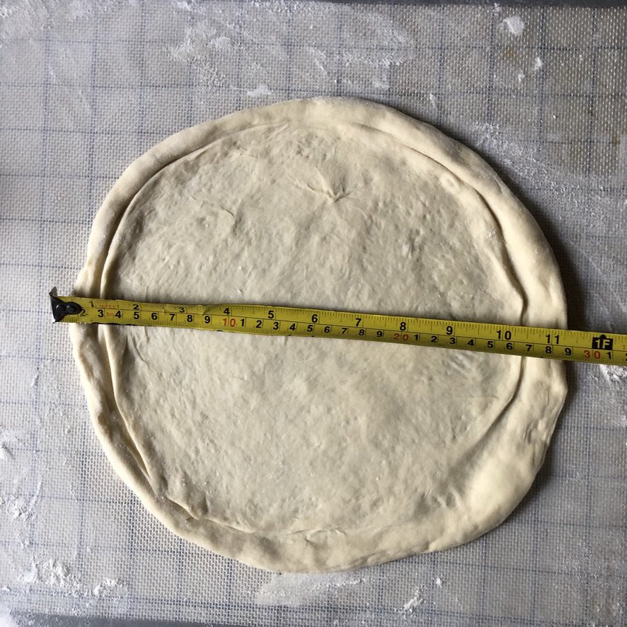 A stretched pizza dough with a measuring tape showing that it's 11 inches in diameter and you can sauce it now or stretch it one more inch.
