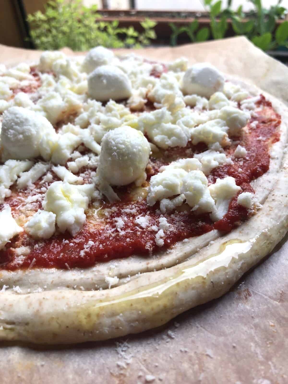 A delicious unbaked assembled whole wheat pizza with easy pizza sauce,fresh mini mozzarella balls, and freshly shredded mozzarella cheese.