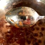 Strawberry-apricot-nectarine jam that's reached gel point showing it coating the back of a spoon and not dripping when a finger has been swiped through it.