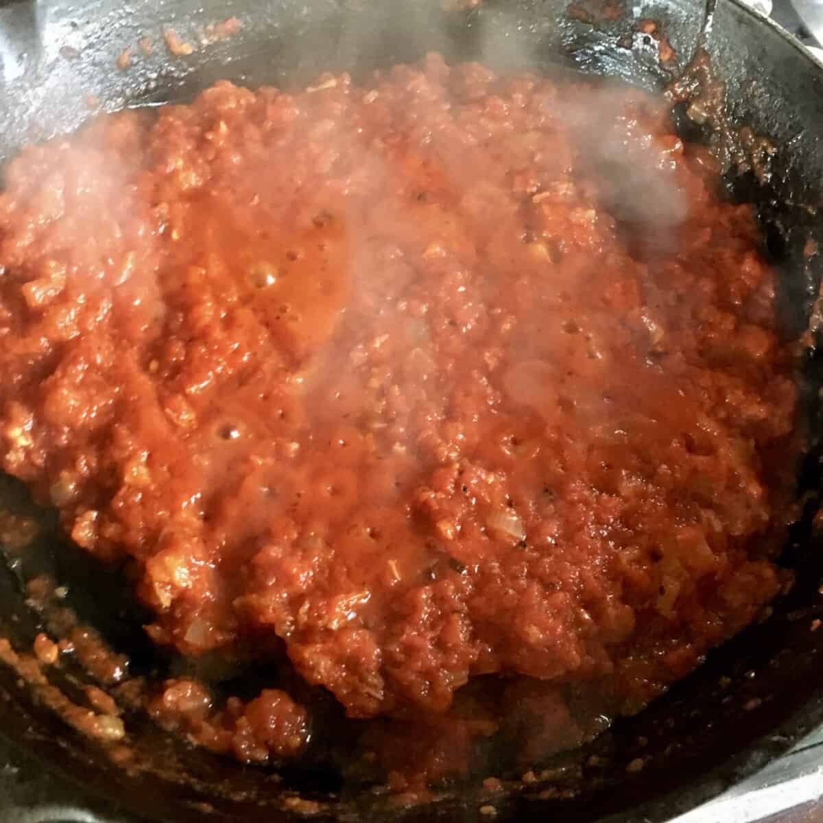 A skillet with pasta sauce in it being cooked to reduce it to pizza sauce consistency.
