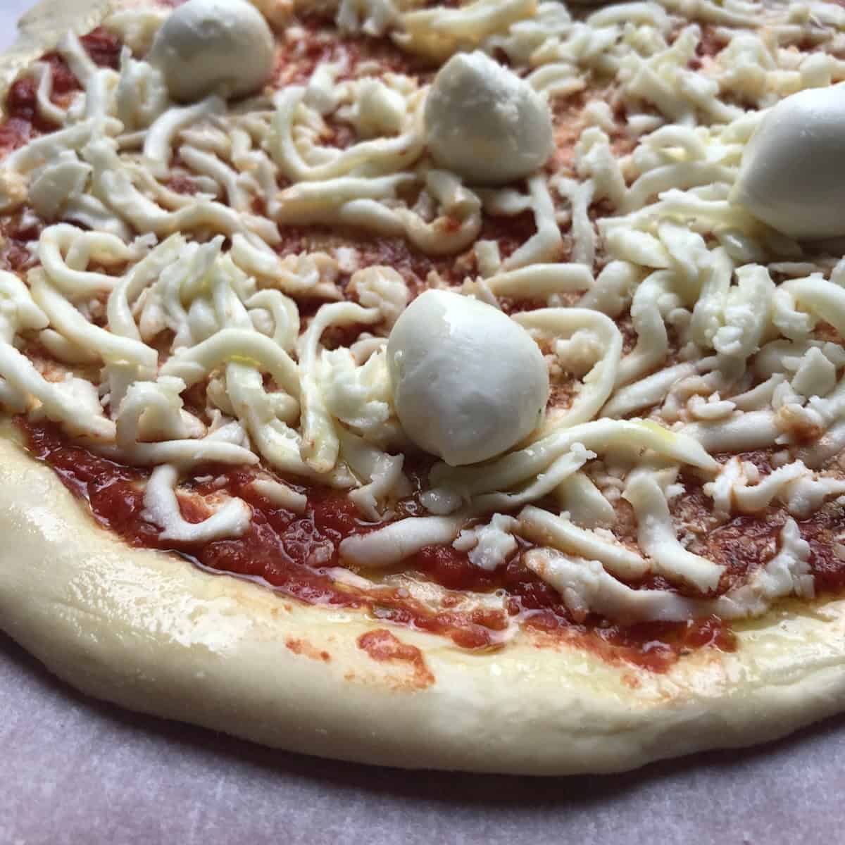 Homemade pizza with thick crust pizza dough topped with tomato sauce, whole milk mozzarella, grana padano, and buffalo mozzarella ready to bake.
