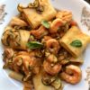 A beautiful bowl of paccheri pasta with shrimp and zucchini in a tomato and white wine sauce.