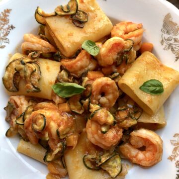 A beautiful bowl of paccheri pasta with shrimp and zucchini in a tomato and white wine sauce.