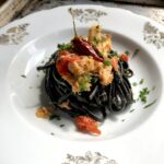 Black linguine pasta with crab and chili in white wine sauce being served.