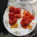 blanched and peeled yellow and red grape tomatoes on a plate next to a pile of tomato skins.
