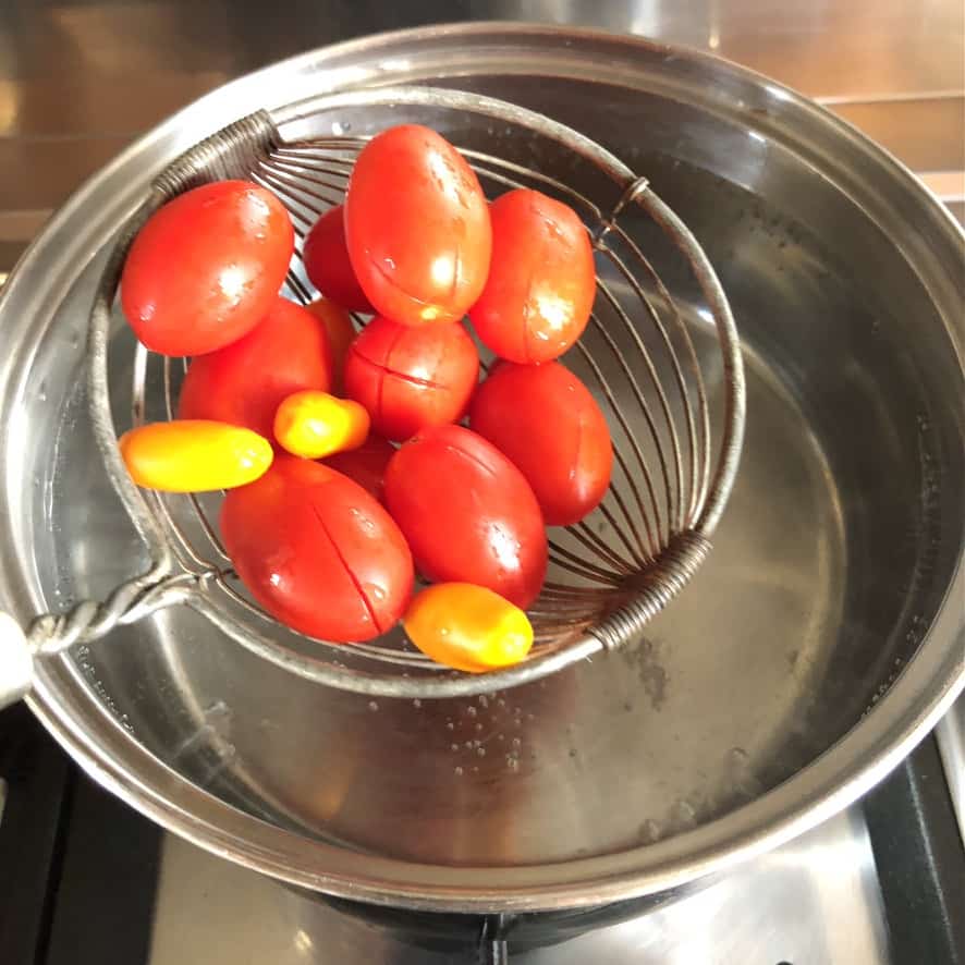 adding scored grape tomatoes to a pot of boiling water to blanch them for about 1 minute.