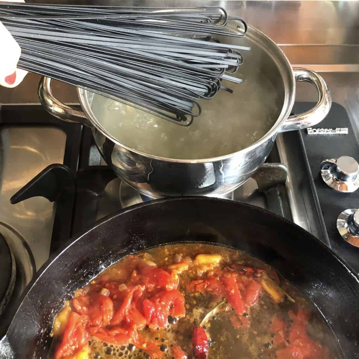 Adding black pasta to a pot of boiling water with the crab sauce cooking in the foreground.