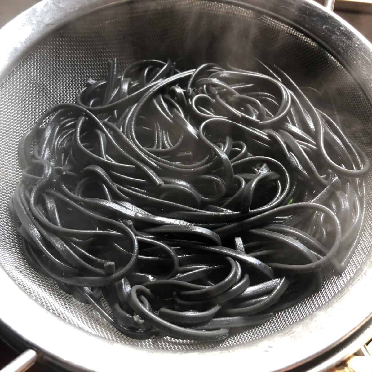 black linguine pasta just cooked and steaming in a sieve.