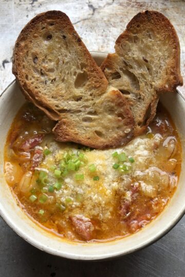 A piping hot bowl of cicerchie and spicy ventricina soup garnished with grated parmesan cheese and chopped chives with 2 pieces of toasted Italian bread tucked into the bowl.