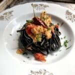 A pasta bowl filled with black squid ink tagliatelle with crab meat sugo and chunks of crab with a hot pepper garnish on top.