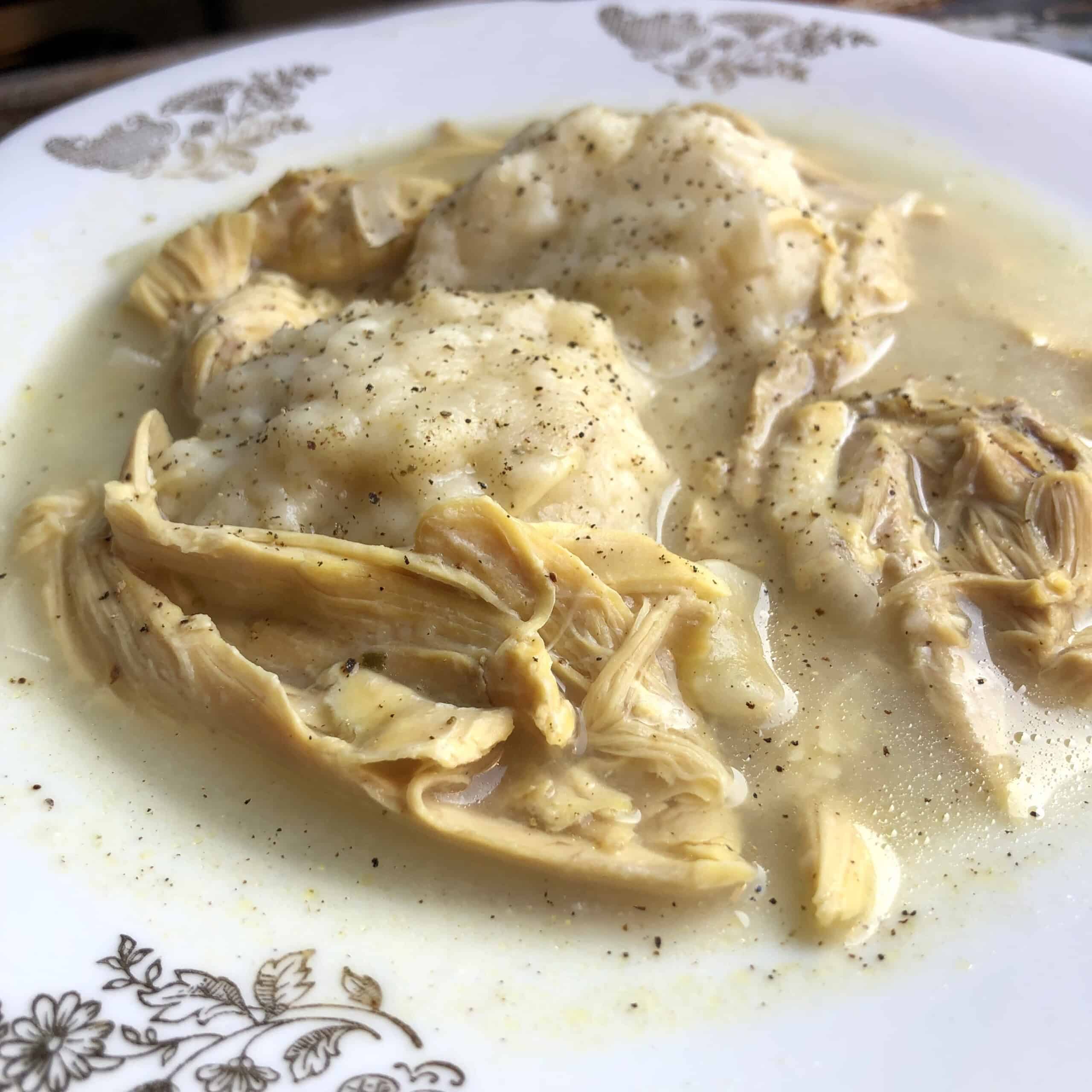 A bowl of southern chicken and dumplings with homemade drop dumplings in a golden broth.