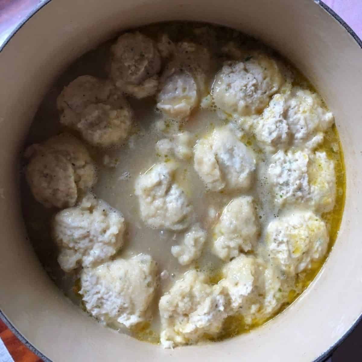 Raw drop dumpling batter covering the entire surface of the chicken and broth in the pot ready to cover and steam.
