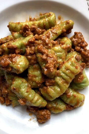 A bowl full of tender spinach gnocchi covered in a meaty bolognese sauce.
