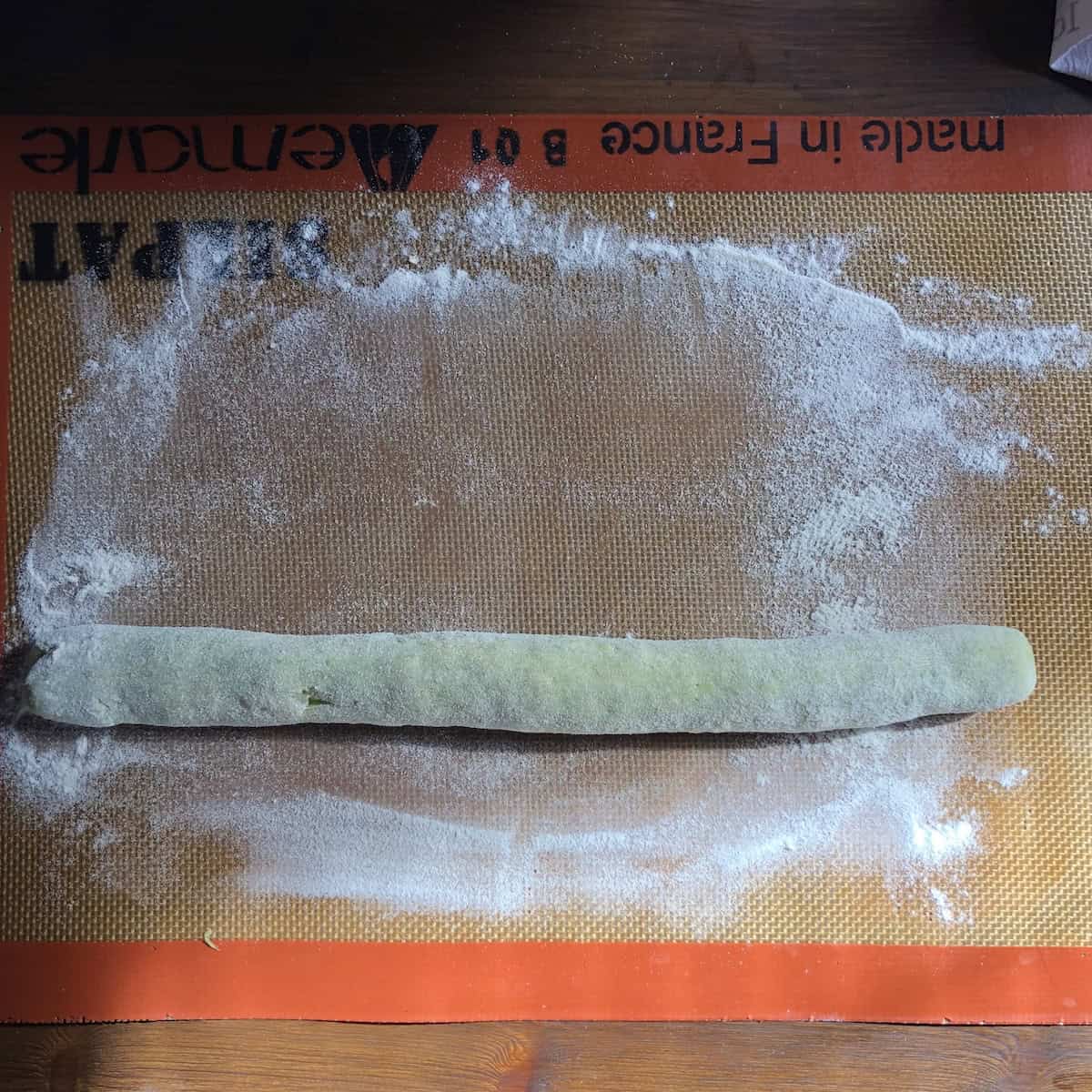 A long spinach gnocchi rope rolled out on a Silpat, best gnocchi recipe technique for even sizing.
