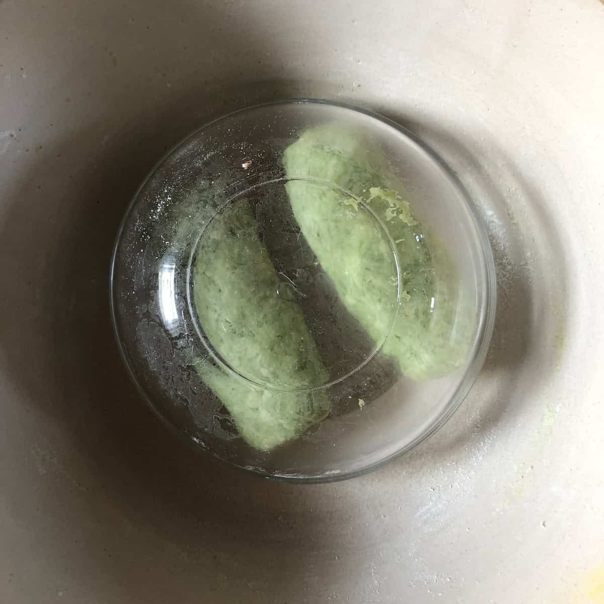 Two spinach gnocchi dough logs resting under a glass mixing bowl to relax before rolling into ropes.
