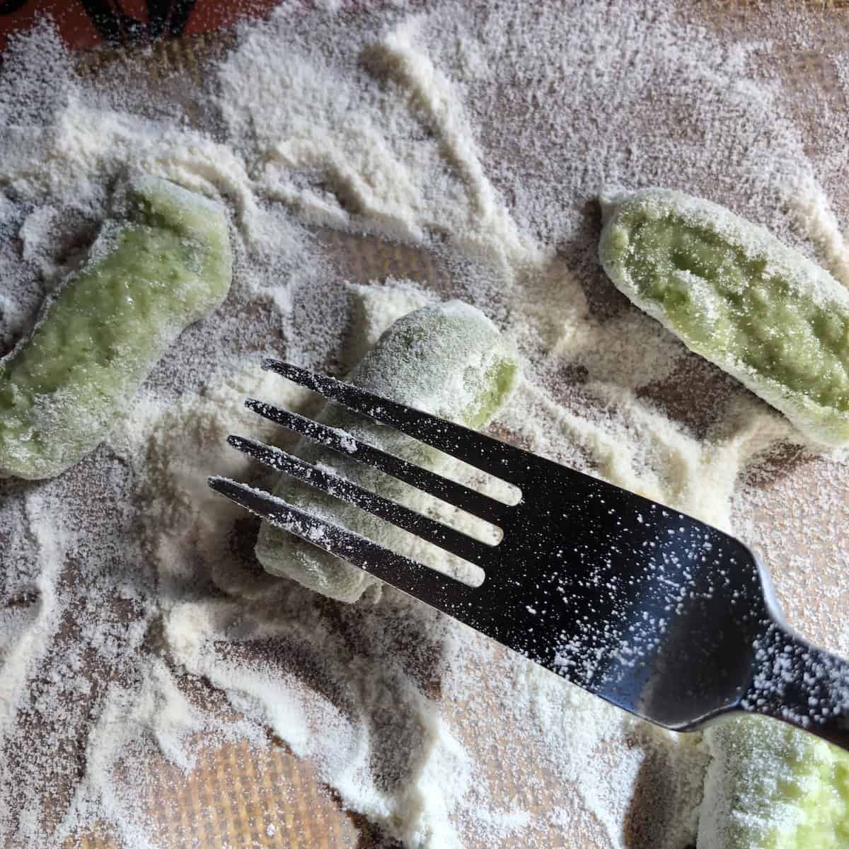 Making ridges on spinach gnocchi using the tines of a fork, gnocchi recipe technique for sauce to cling to each piece.

