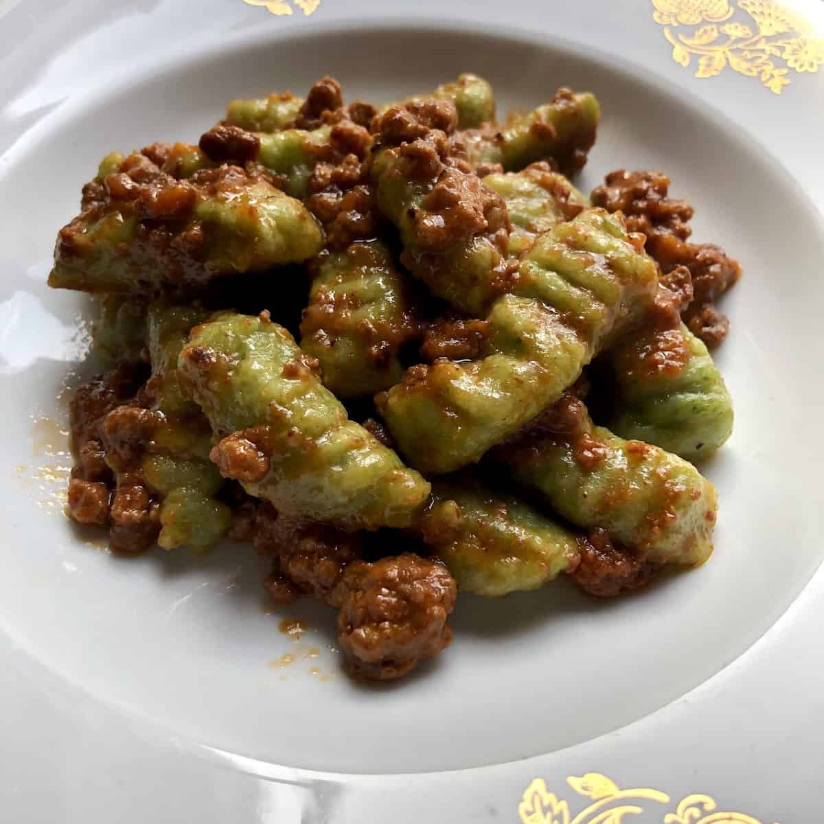 Plated spinach gnocchi bolognese with a rich ragu sauce, made with homemade spinach gnocchi from scratch.