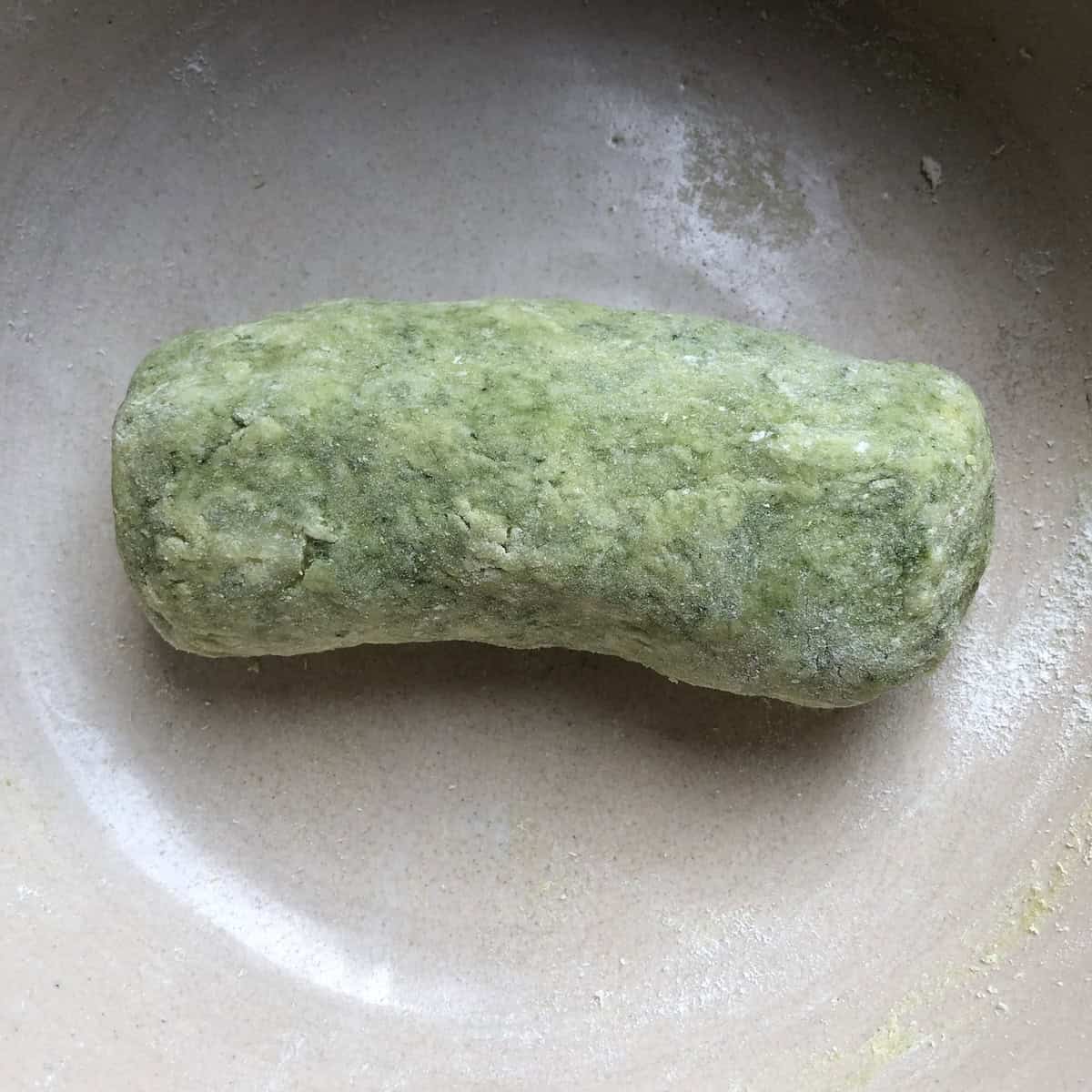 A green spinach gnocchi dough log on a floured surface, homemade gnocchi ready to portion.
