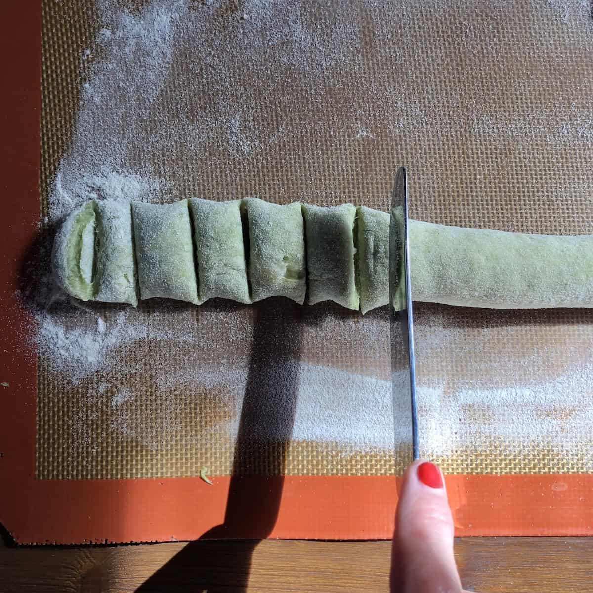 Cutting spinach gnocchi from the rope using a butter knife, how to make gnocchi at home with even portions.
