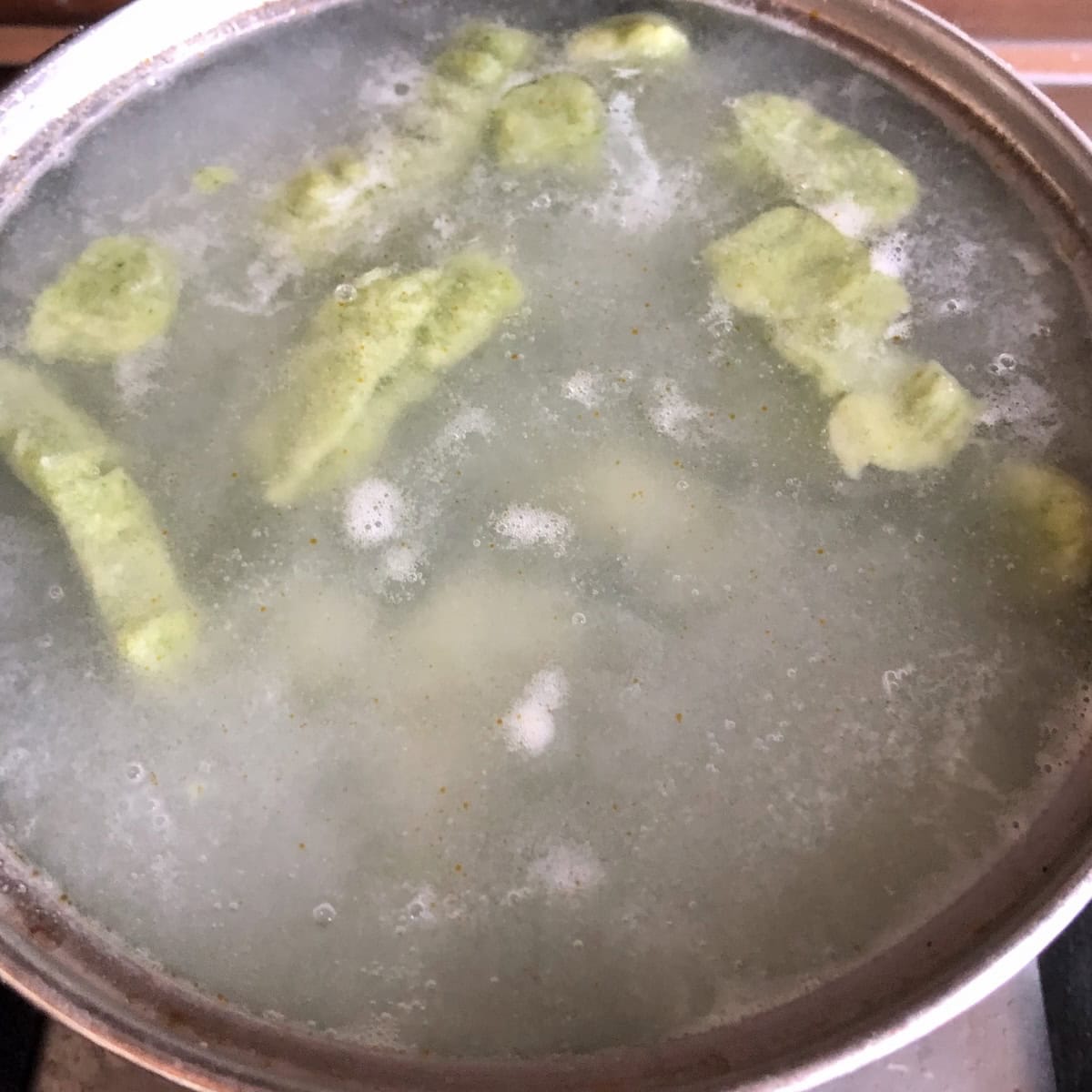 A pot of boiling homemade spinach gnocchi cooking until they float, how to cook gnocchi from scratch.
