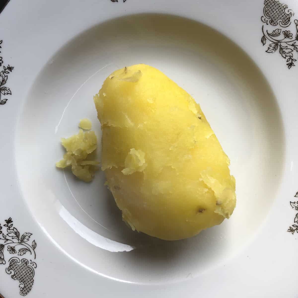 A single boiled potato with skin removed using a spoon still hot and ready for making spinach gnocchi, potato gnocchi recipe first step.
