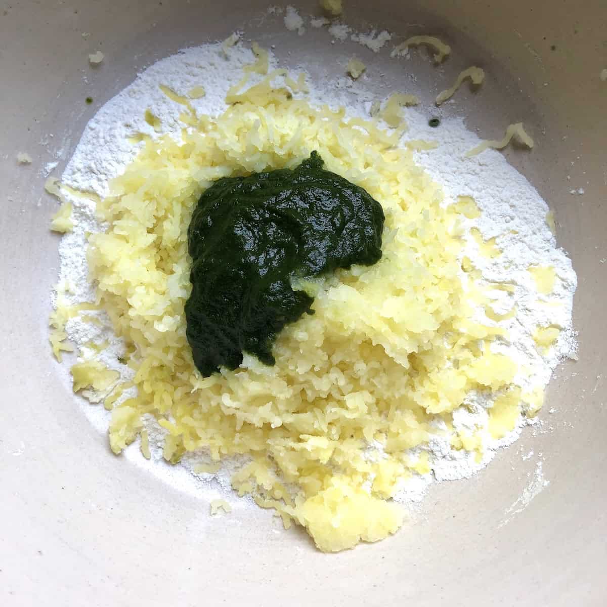 00 flour, riced potato, and spinach added to a large mixing bowl for a homemade spinach gnocchi recipe.
