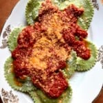 Fresh homemade green spinach and ricotta ravioli filled with ricotta cheese, spinach, and parmigiano-reggiano cheese arranged on a platter with bright tomato pomodoro sauce.