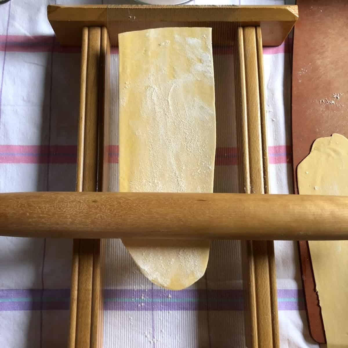 Rolling a sheet of semolina egg pasta on a chitarra tool using a rolling pin to cut the pasta on the carbon steel strings, chitarra pasta maker in action.
