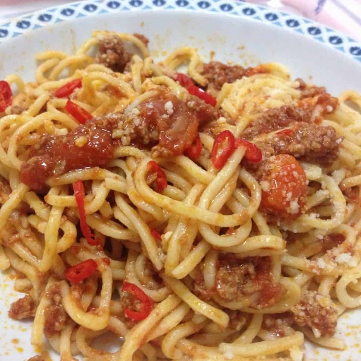 Closeup of a bowl of spaghetti alla chitarra with spicy sausage tomato sauce topped with spicy red pepper slices that we cut using kitchen scissors at the table as desired for a traditional pasta alla chitarra from zia Linda in Abruzzo ready to eat.