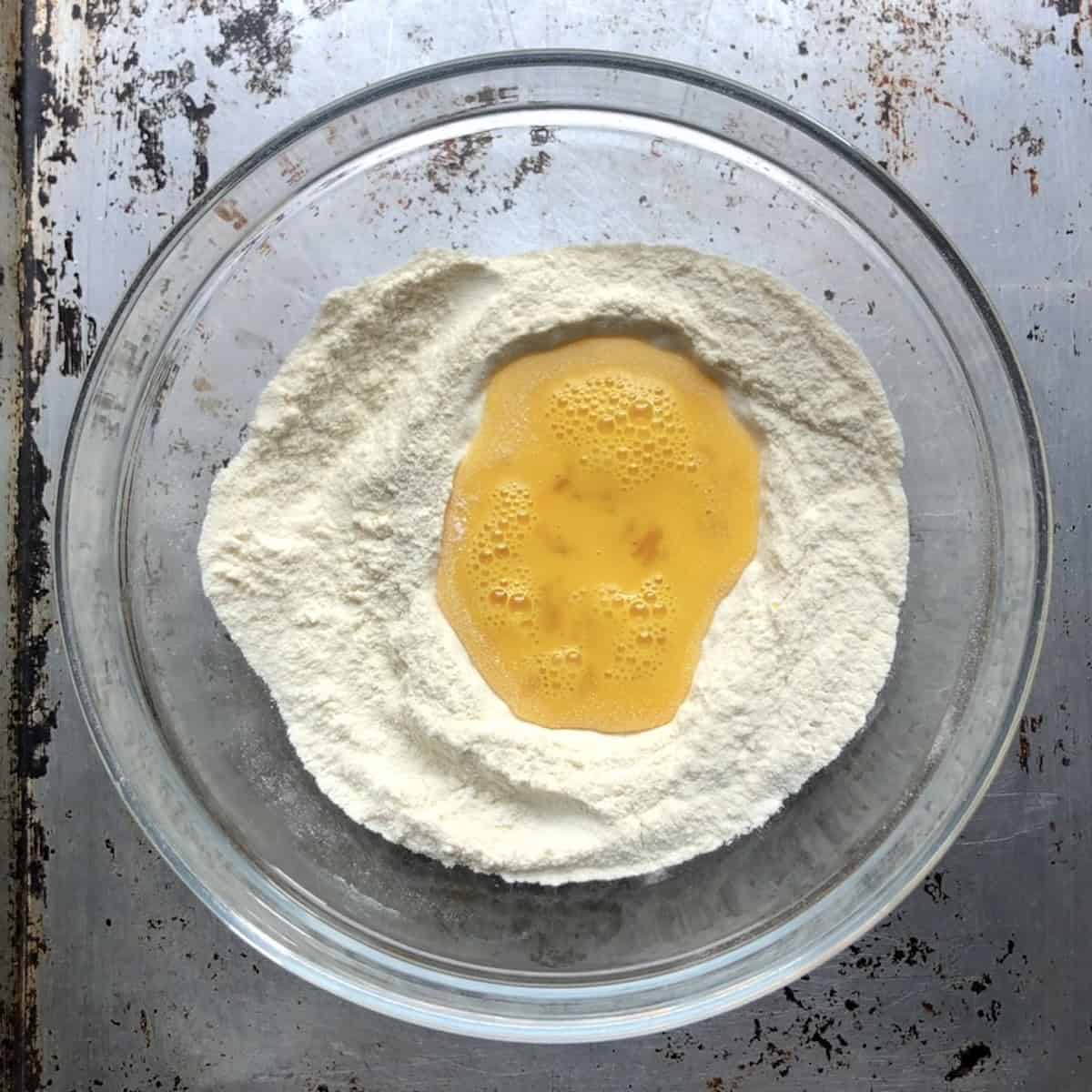 Semola rimacinata flour in a mixing bowl with whisked eggs in the center well, chitarra pasta recipe first step.
